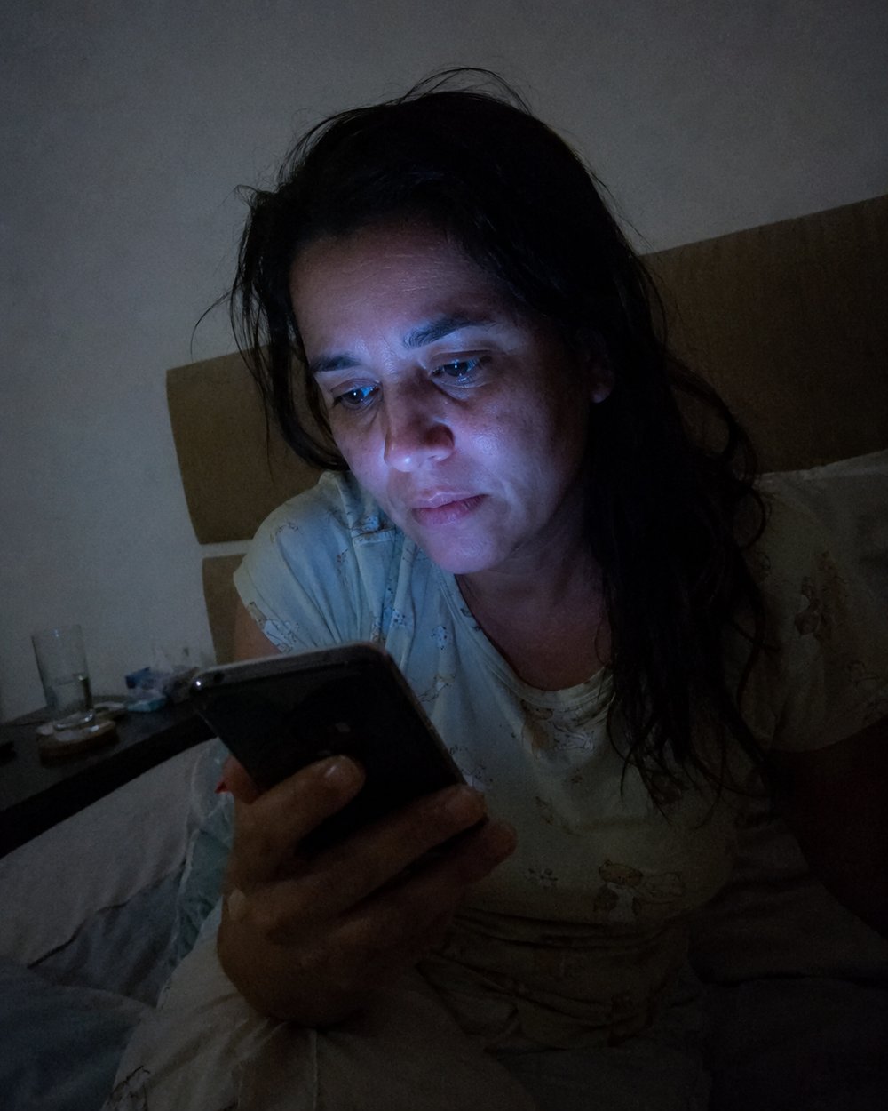 Mulher pesquisando sintomas no celular na madrugada, no escuro